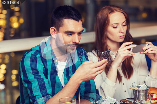 Image of couple with smartphones dining at restaurant