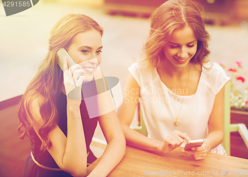 Image of happy young women with smartphones at outdoor cafe