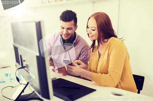 Image of happy creative team with smartphones at office