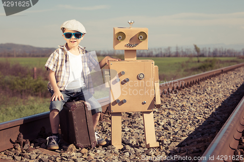 Image of Happy little boy and robot walking with suitcase on the railway 