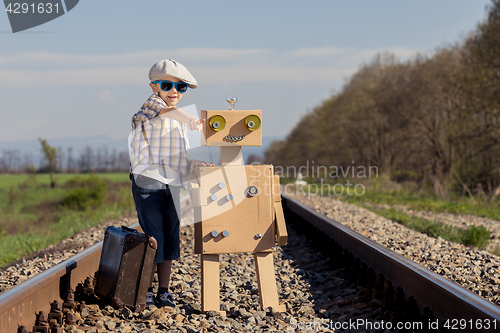 Image of Happy little boy and robot walking with suitcase on the railway 