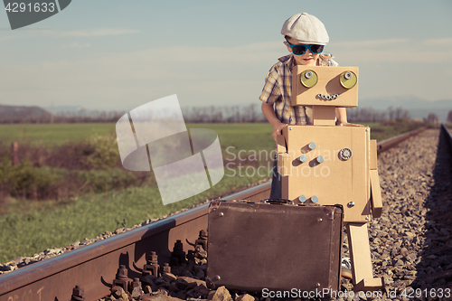 Image of Happy little boy and robot walking with suitcase on the railway 