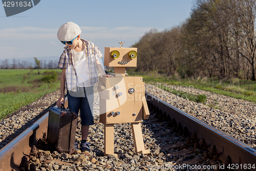 Image of Happy little boy and robot walking with suitcase on the railway 