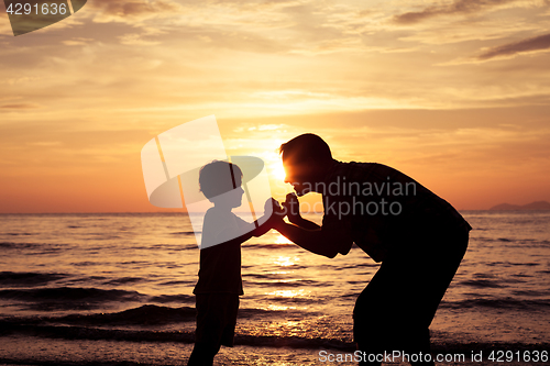 Image of Father and son playing on the beach at the sunset time.