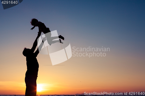 Image of Father and son playing on the beach at the sunset time.