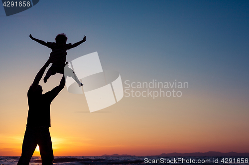 Image of Father and son playing on the beach at the sunset time.