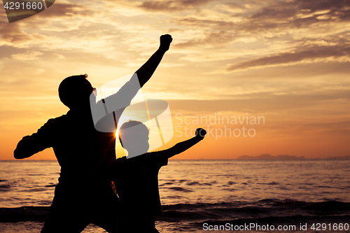 Image of Father and son playing on the beach at the sunset time.