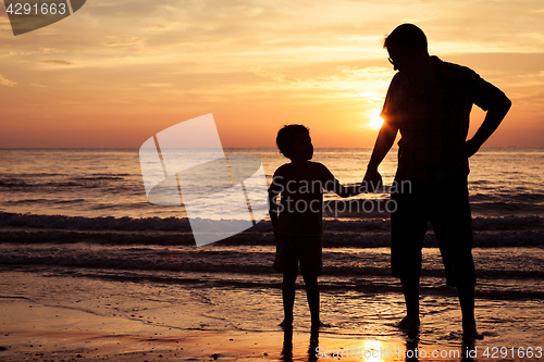 Image of Father and son playing on the beach at the sunset time.