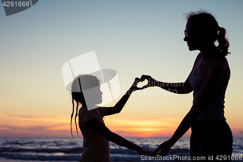 Image of Mother and daughter playing on the beach at the sunset time.