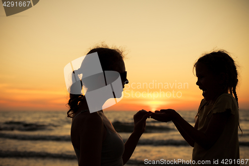 Image of Mother and daughter playing on the beach at the sunset time.