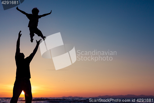 Image of Father and son playing on the beach at the sunset time.