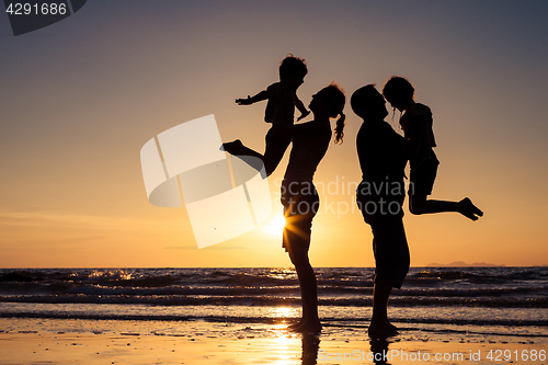 Image of Silhouette of happy family who playing on the beach at the sunse