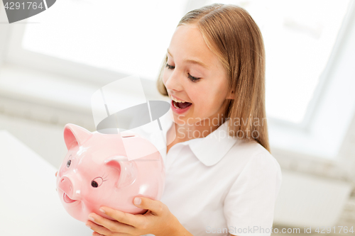Image of happy girl with piggy bank at home