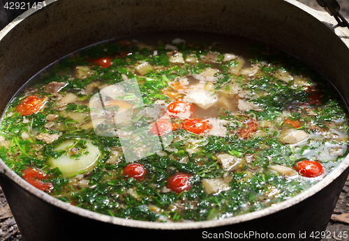 Image of Freshly cooked hot soup in sooty cauldron on camp fire