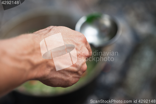 Image of Man\'s hand with metal ladle (spoon) and soup in cauldron at back