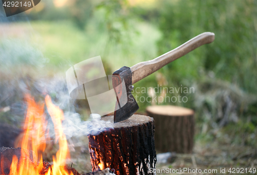 Image of Axe in tree stump and campfire with smoke