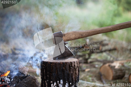 Image of Axe in tree stump and campfire with smoke