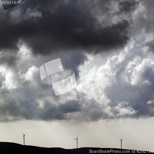 Image of Silhouette of wind farm and overcast cloudy sky before storm