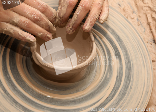 Image of Woman in process of making clay bowl on pottery wheel