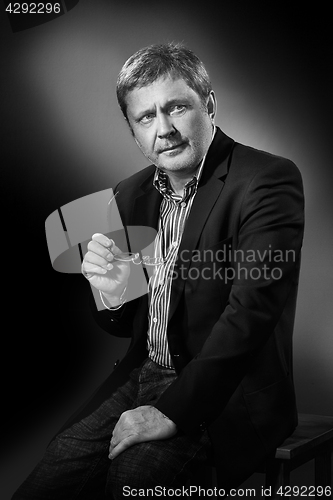 Image of Handsome pensive mature businessman in formal suit is looking while sitting on chair, on gray background