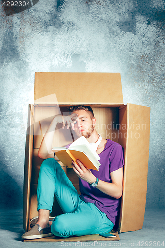 Image of Introvert concept. Man sitting inside box and reading book