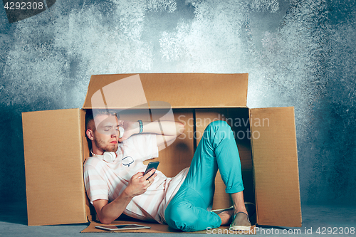 Image of Introvert concept. Man sitting inside box and working with phone