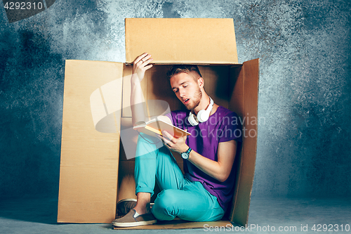 Image of Introvert concept. Man sitting inside box and reading book