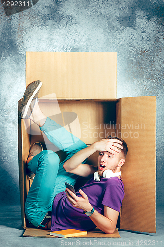 Image of Introvert concept. Man sitting inside box and working with phone