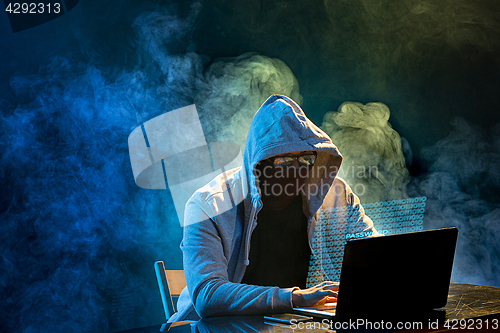 Image of Hooded computer hacker stealing information with laptop