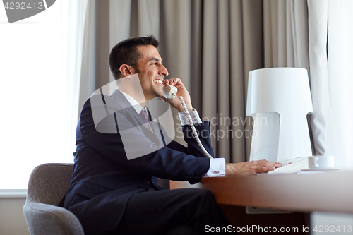 Image of businessman calling on desk phone at hotel room