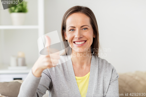 Image of happy smiling woman showing thumbs up at home