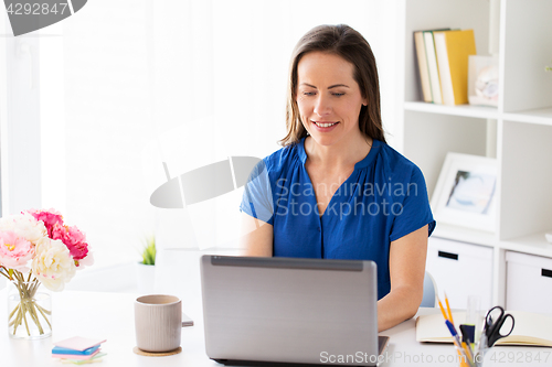 Image of happy woman with laptop working at home or office