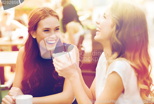 Image of smiling young women with coffee cups at cafe