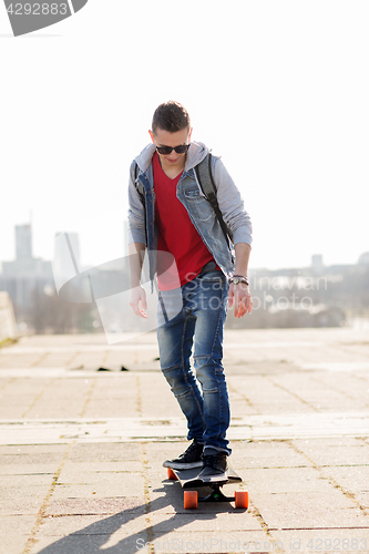 Image of happy young man or teenage boy riding on longboard