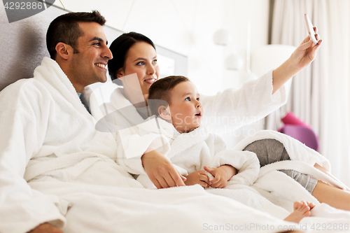 Image of happy family with smartphone in bed at hotel room