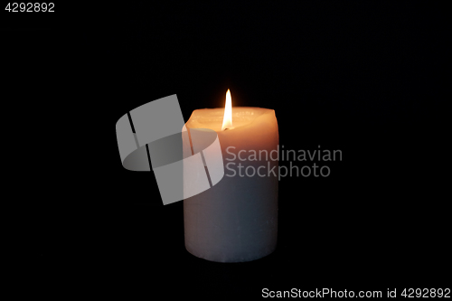 Image of candle burning in darkness over black background