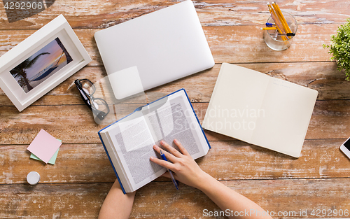 Image of hands of woman reading book at wooden table