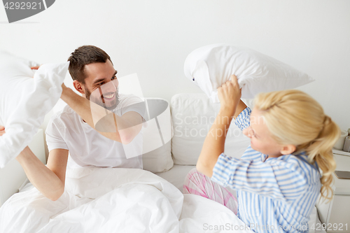 Image of happy couple having pillow fight in bed at home