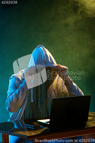 Image of Hooded computer hacker stealing information with laptop