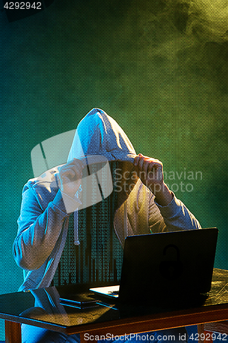 Image of Hooded computer hacker stealing information with laptop