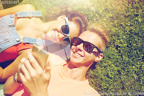 Image of happy teenage couple smartphone lying on grass