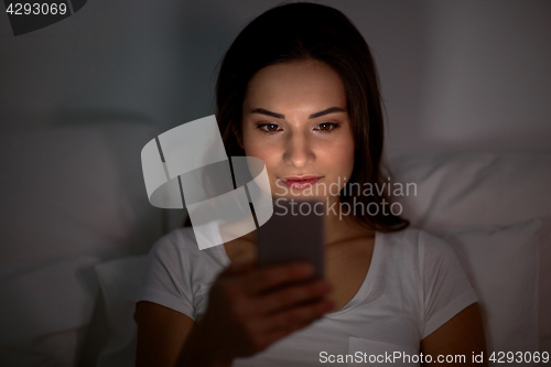 Image of happy young woman with smartphone in bed at night