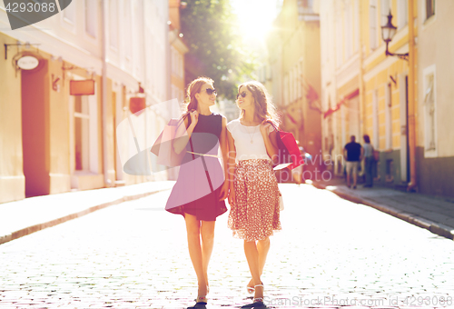 Image of happy women with shopping bags walking in city