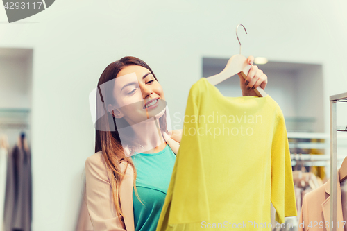 Image of happy young woman choosing clothes in mall