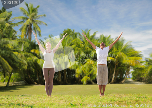 Image of happy couple making yoga exercises on beach