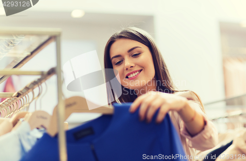 Image of happy young woman choosing clothes in mall