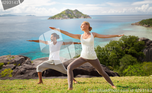 Image of couple making yoga in warrior pose at seaside