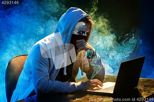 Image of Hooded computer hacker stealing information with laptop