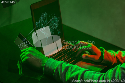 Image of Hooded computer hacker stealing information with laptop