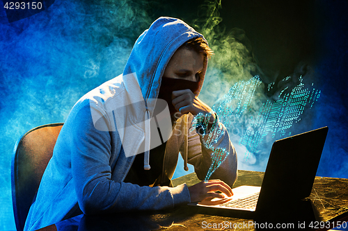 Image of Hooded computer hacker stealing information with laptop